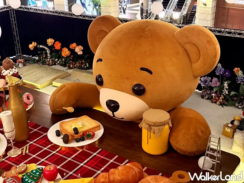 ▲巨型熊熊趴在超大餐桌上，專注凝視放大版甜點與麵包，細節精緻宛如童話佈景。