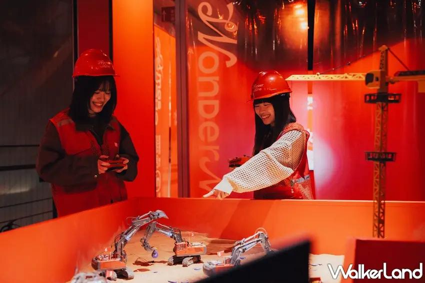 ▲民眾戴上工程帽,在紅色沉浸式空間中專注操作遙控挖土機,體驗挖掘禮物鑰匙的樂趣