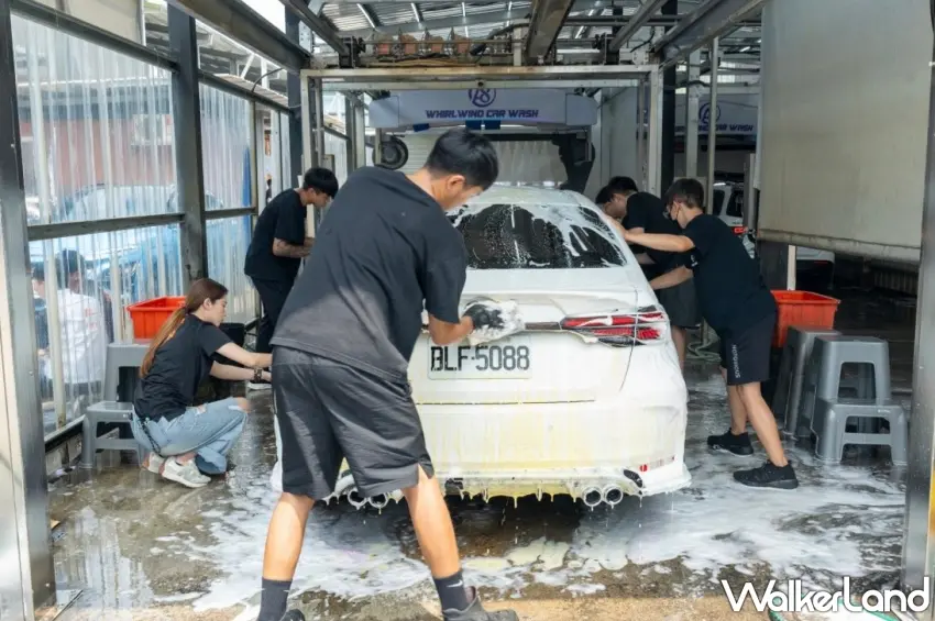 ▲多位志工圍繞著白色轎車進行精細的人手洗車，在噴淋設備下分工合作完成清潔任務。圖／A8旋風洗車中心提供；窩客島整理