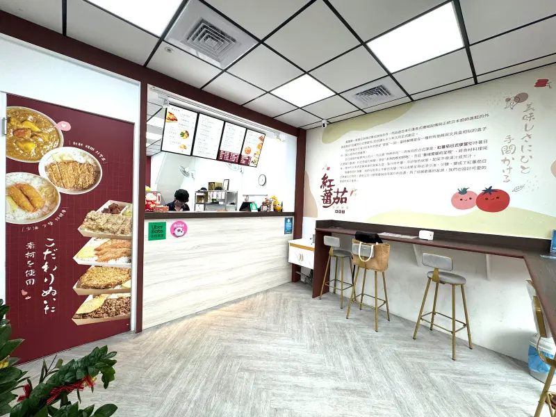 紅蕃茄日式便當的店內環境，裝潢以木質紋理的櫃檯為主，搭配簡約的高腳椅，整體空間潔淨整齊，營造出溫馨且充滿日式風情的氛圍，主要提供顧客外帶等候使用。