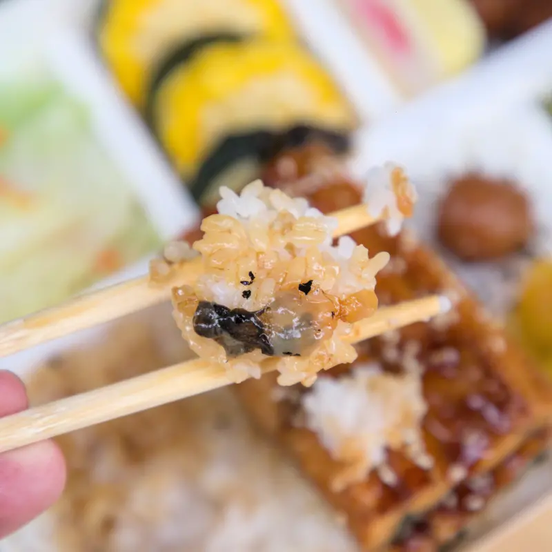 紅蕃茄鰻魚飯的米飯特寫，每一顆飯粒都吸飽了蒲燒醬汁的精華，呈現誘人的焦糖色，醬汁的香氣與米飯的Q彈完美結合，讓人難以抗拒。