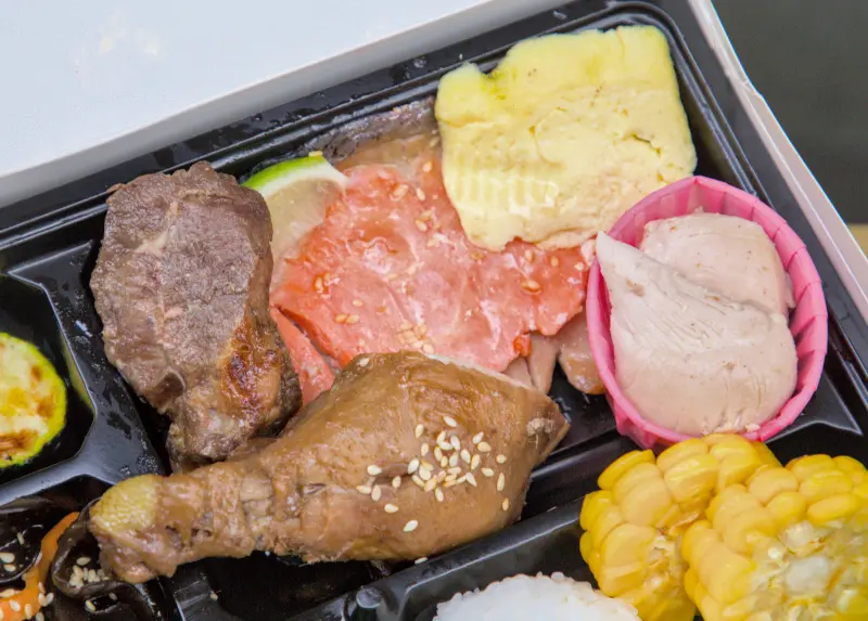 400元客製化便當的近距離特寫，展示便當內豐富的主菜，包含羊排、滷雞腿、鮭魚、烤櫛瓜等，強調其多樣化的頂級用料。