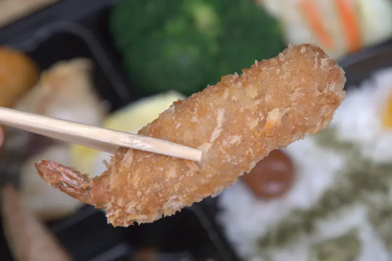 紅蕃茄小資便當中的琵琶蝦特寫，在日文裡稱作「海老」，象徵長壽。蝦子外型飽滿，裹上薄脆麵衣酥炸，蝦肉Q彈緊實，為便當增添豐富的海陸風味。