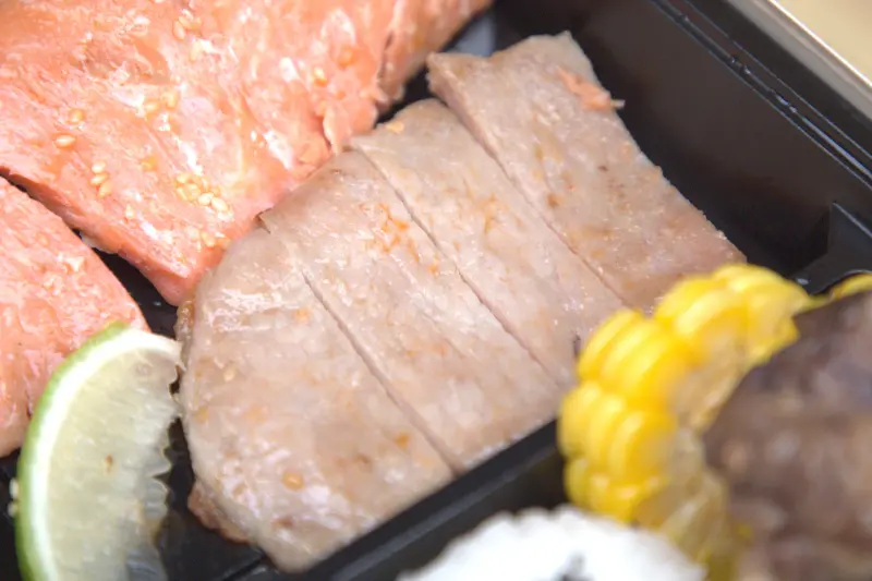 紅蕃茄客製化便當中的鹽烤豬排特寫，豬排以日式簡約手法烤製，外皮微焦酥脆，內部肉質柔嫩多汁，僅用海鹽提味，便能帶出豬肉本身的鮮甜，感受食材最純粹的魅力。