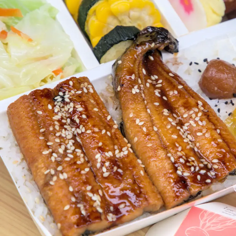 紅蕃茄鰻魚飯的蒲燒鰻魚近照，淋上特製醬汁後金黃油亮，灑上白芝麻增添香氣，看起來美味可口，展現日式蒲燒料理的精髓。