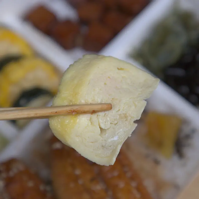 紅蕃茄鰻魚飯的日式玉子燒特寫，口感鬆軟綿密，帶有淡淡蛋香與高湯的甘甜，是便當裡不可或缺的日式小菜。